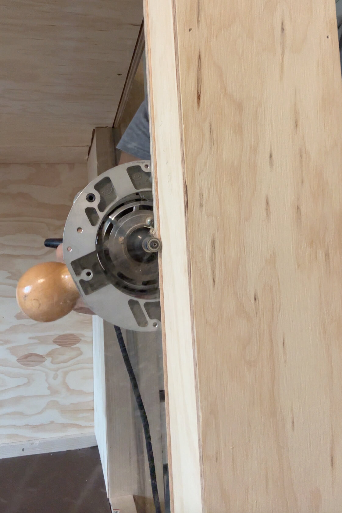 Using a router to clean up the uneven edges of plywood on a bunk bed frame.